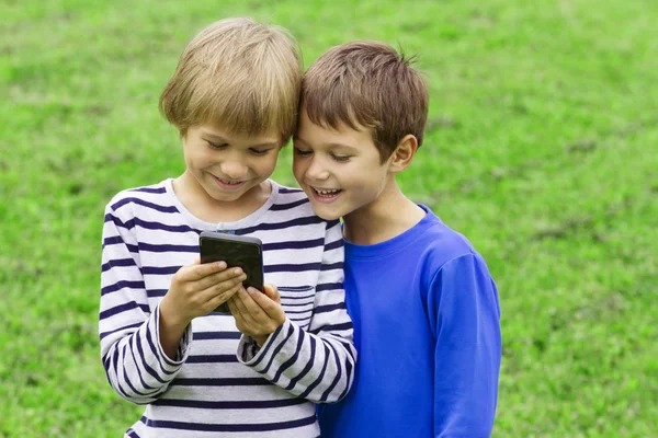 Children with mobile phone. Two boys smiling, looking to screen, playing games or using application. Outdoor. Technology education leisure people concept