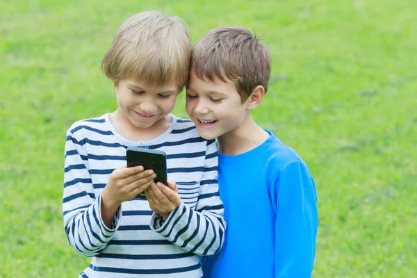 Children with mobile phone outdoor. Two boys smiling, looking to screen, playing games or using application. Technology education leisure people concept