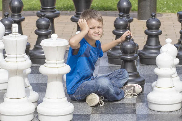 Boy playing chess game and thinking about his next move during an outdoor chess game using life sized pieces and board