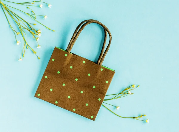 Small white meadow flowers and polka dot paper bag  on blue background. Copy space. Flat lay. Top view