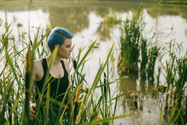 Young beautiful girl with blue hair looks stare predator reed bushes