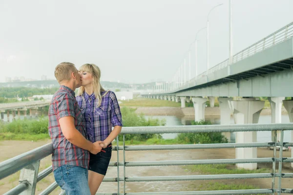 Man and woman in the plaid shirt kiss cute embracing standing on the stairs of the bridge