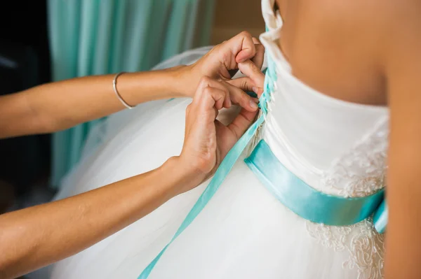 Bridesmaid helps to tie a bow on a festive white dress of the bride on the wedding day