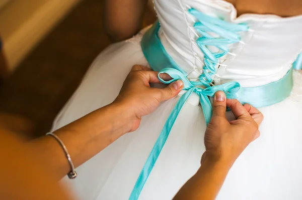 Bridesmaid helps to tie a bow on a festive white dress of the bride on the wedding day