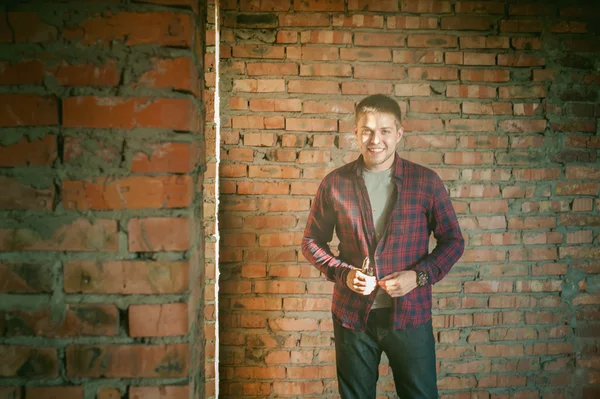 Man in a plaid shirt and jeans, smokes an electronic cigarette, blowing smoke and steam from the vaporization a mechanical device. location Abandoned unfinished building, brick walls, stylish.