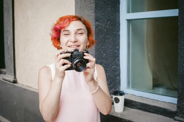 Portrait of a girl with a camera. woman with dyed red hair in a pale pink dress derzhet holding vintage camera