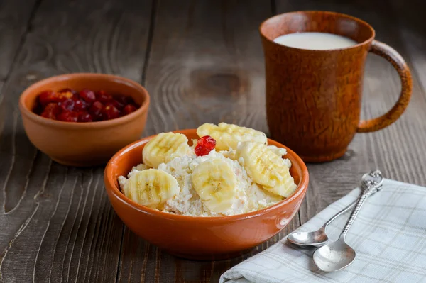 Cottage cheese in color bowl with banana and cherry on wood back