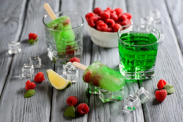 Green Ice Cream Popsicle with Lime and raspberry on a wooden table