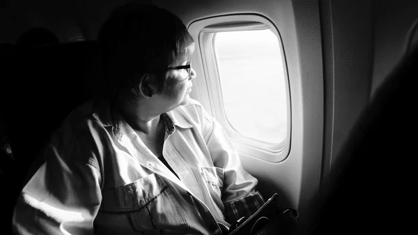 Female airplane passanger seeing out of airplane cabin window, black and white high contrast picture style, highlight on woman middle of picture