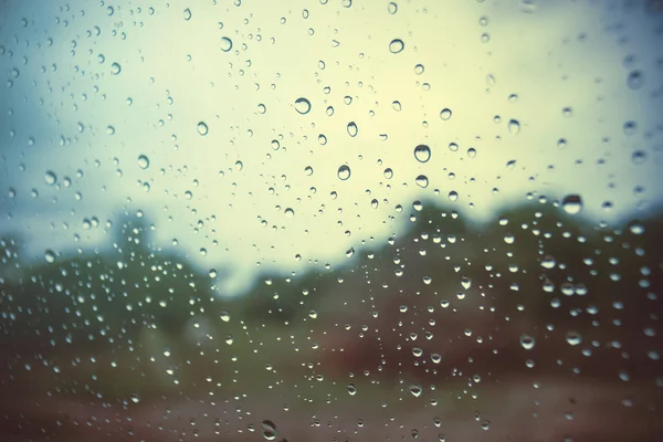 Water drop of rain on a glass, blurred sun with blue sky and cloud in background, selective focus, low contrast picture style,fitered image with vintage grainy film styl