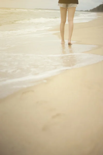 Beach travel - young woman walking on sand beach leaving footprints in the sand. Closeup detail of female feet and white sand,filtered image, selective focus on woman,warm white balance picture style,light effect added