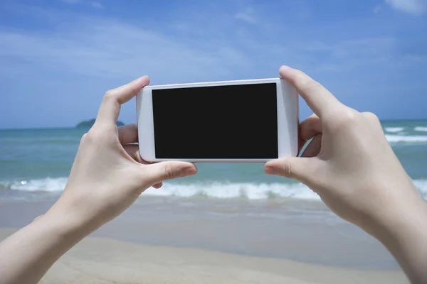 Close up of woman's hand holding smartphone, mobile, smart phone over blurred beautiful blue sea to take a photo of the sea,phone with black scree