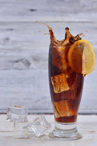 Lemon slice splashes in a full of cola and ice cubes glass