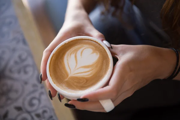 Female hand holding cup of coffee with heart shape