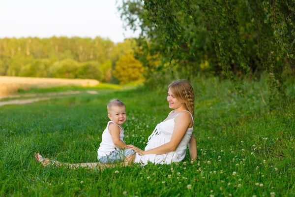 Pregnant mom with a boy resting in a meadow.