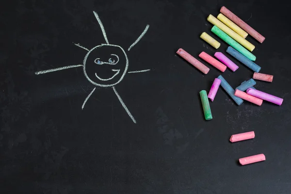 Colored chalks, black blackboard with drawings of the sun