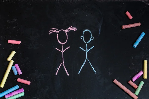 Colored chalks, black blackboard with the drawings of little girl and boy