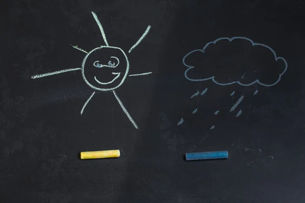 Colored chalks, black blackboard with drawings of sun and a cloud