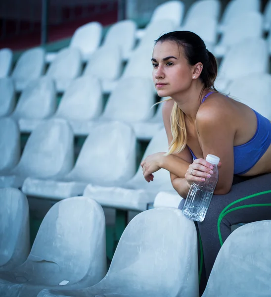 Young sporty woman drinking water after running in the stadium, close-up