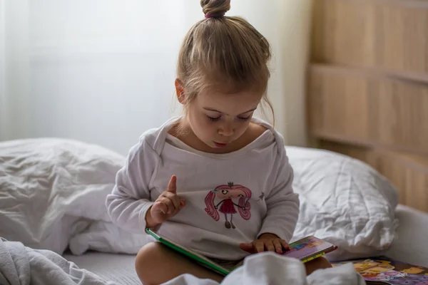 Little girl reads a children\'s book in bed after sleep