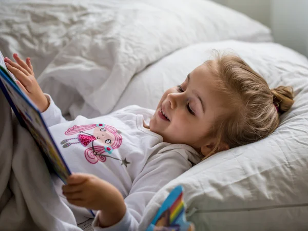 Little girl reads a children's book in bed after sleep