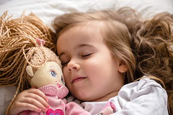 Little girl falls asleep in bed with soft doll white