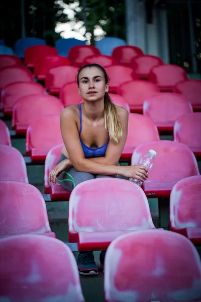 Young sporty woman drinking water after running in the stadium, close-up