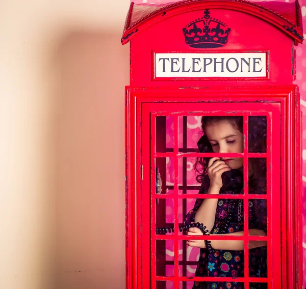 Little girl hides and plays in a traditional red telephone booth