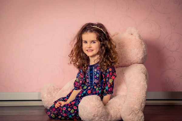 Little girl plays big soft bear in a baby pink room