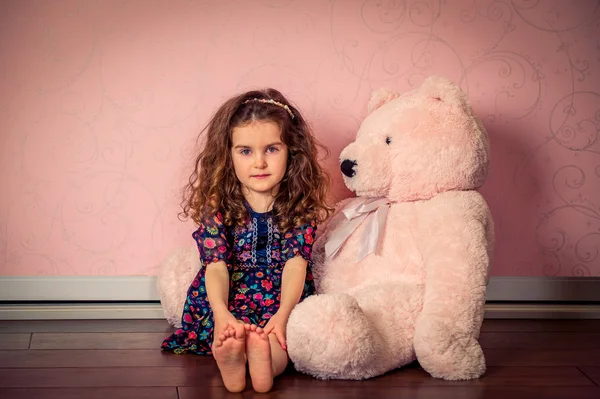 Little girl plays big soft bear in a baby pink room