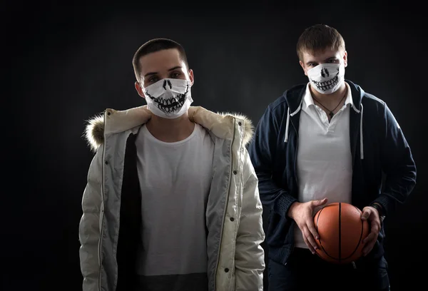 Studio on a black background portrait of two men in masks with basketball