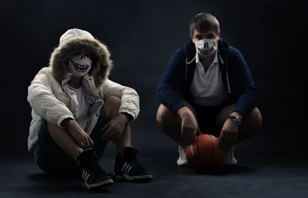 Studio on a black background portrait of two men in masks with basketball