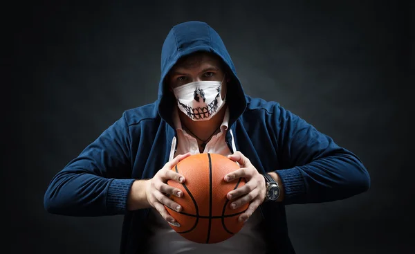 Studio on a black background portrait of guy in mask with basketball