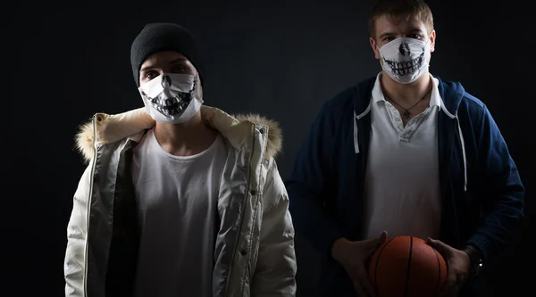 Studio on a black background portrait of two men in masks with basketball