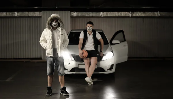 Portrait of two men in the parking lot next to the car with a basketball in masks