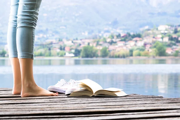 Young girl lies on a pier and reading a book on bare feet