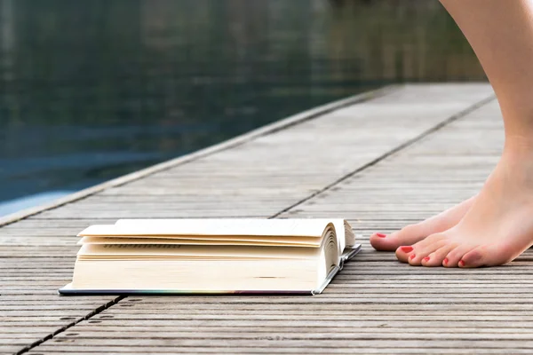 Girl bare feet with red nail polish on a wooden pier net to a book on a wooden pier