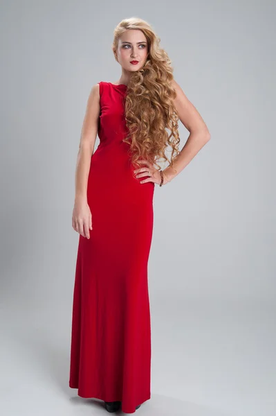Beautiful girl in a long red dress with long curly hair holding