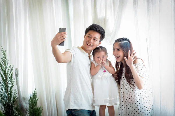 Family with little girl in park taking selfie by mobile phone.