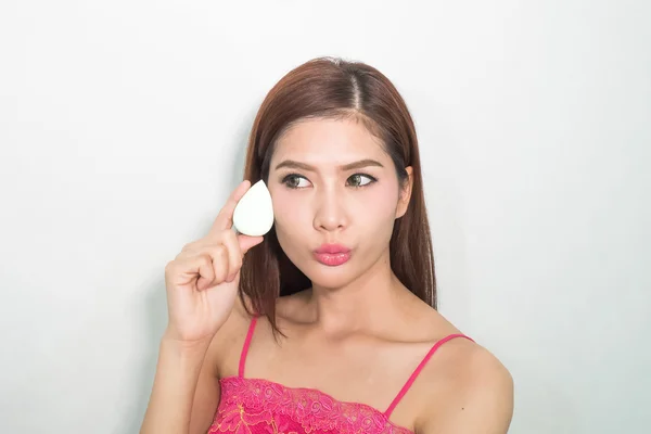 Beautiful young woman applying foundation to face with green egg