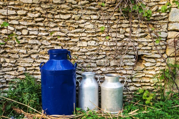 Three milk cans in front of stone background