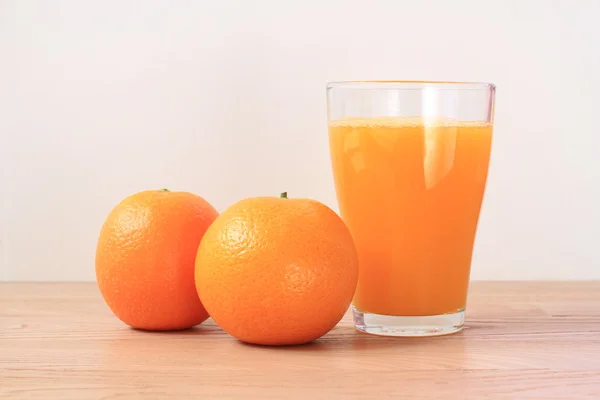 Glass of orange juice with two oranges, on a table in a living room