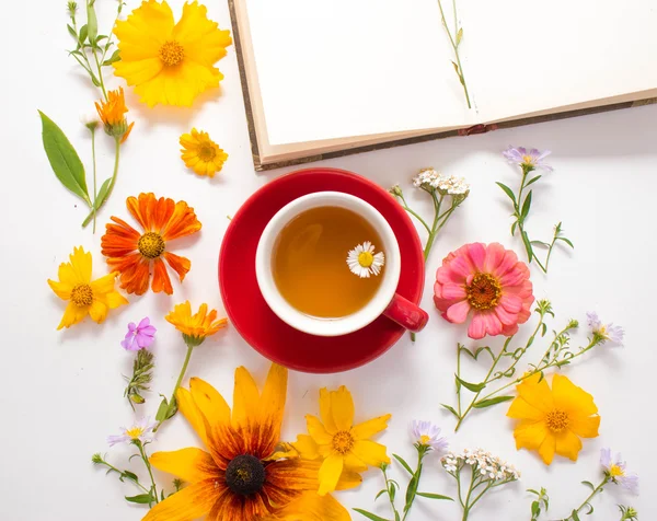 Flowers, a mug with herbal tea, a notebook on a white background.