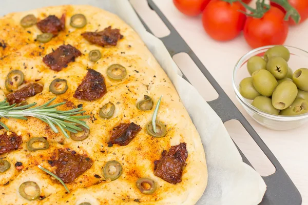 Freshly baked traditional Italian focaccia bread with green olives and sun-dried tomatoes