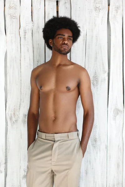 Fashion photo of african american athletic man with sport wet body is posing near the texture wall background