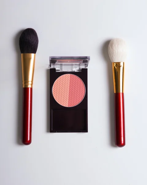 Golden cosmetics - powder, blusher, brush on light wooden background with copy space. Top view, flat lay.