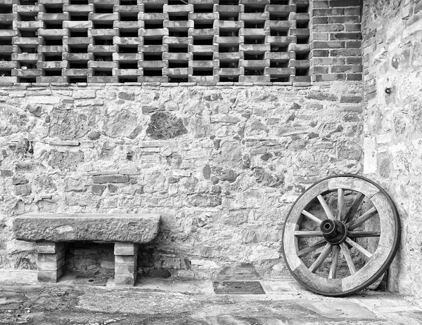Italian house glimpse, stone bench and old wagon wheel