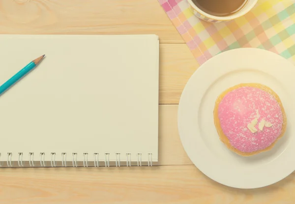 Strawberry Donut with notebook in vintage tone. Donut on plate with cup of coffee with writing equipment.
