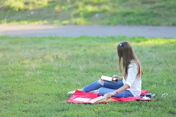 Young girl sitting on the grass in the park works at a laptop and eating fast food