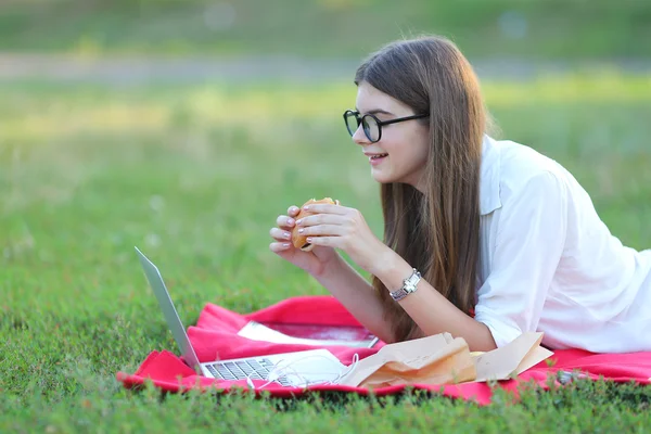 Young girl on the nature of eating fast food and working at a laptop